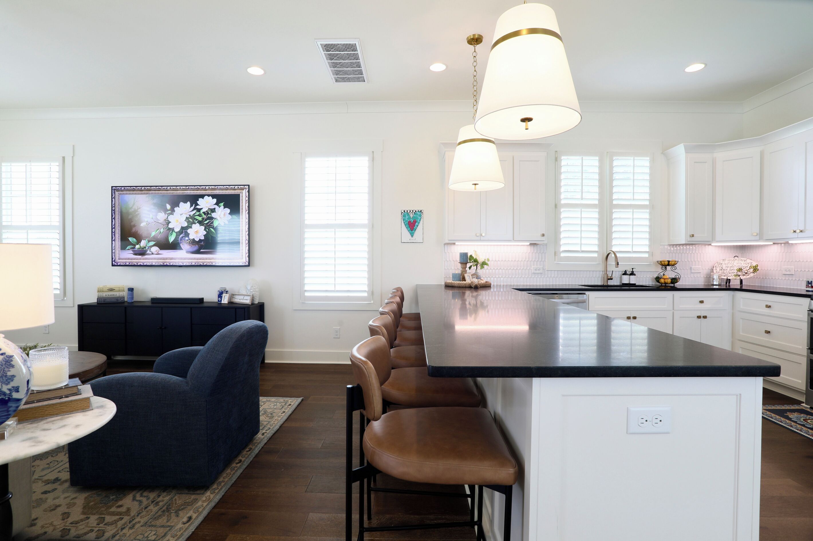 Una cocina moderna con armarios blancos, una isla central con taburetes y luminarias colgantes.