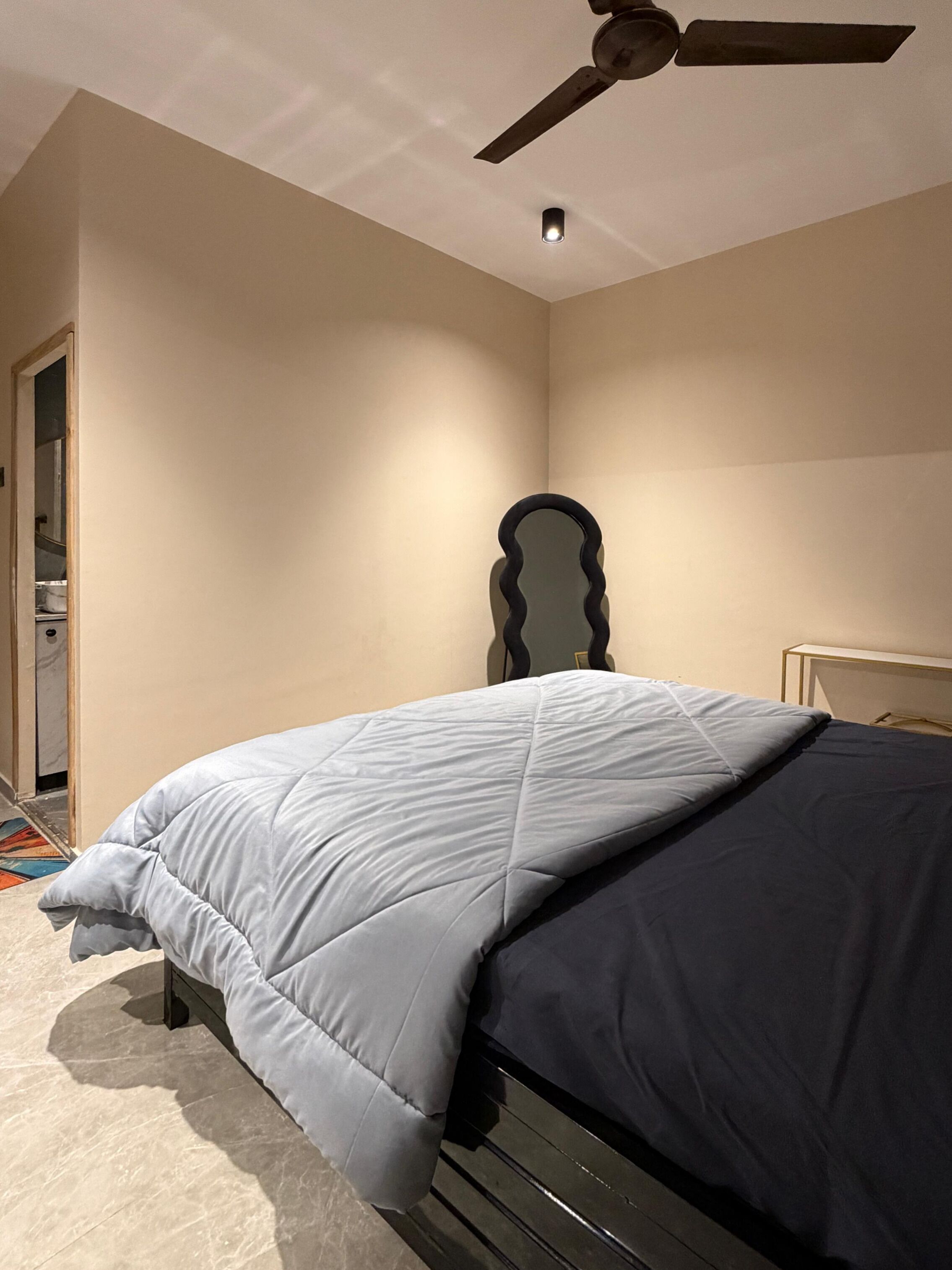 Et soveværelse med seng, ventilator og spejl.