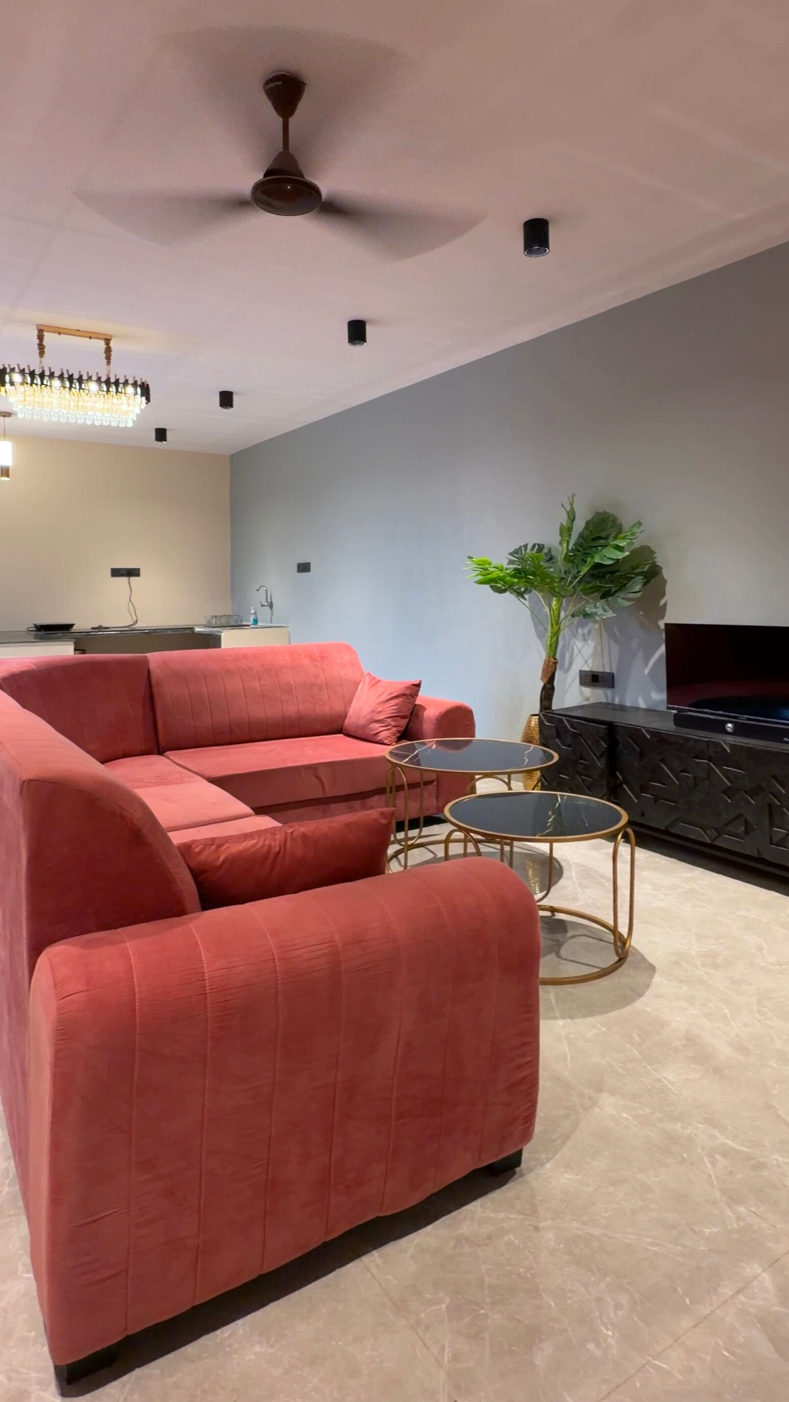 Ein modernes Wohnzimmer mit einer Eckcouch, einem kleinen Couchtisch, einem Fernseher und einem Deckenventilator.