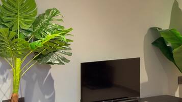 A room with a flat-screen TV mounted on a wall, a black entertainment unit with a gold circular table, and a large green plant.