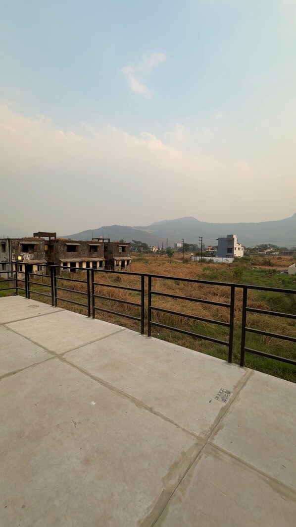 Un balcón de concreto con barandal de metal que da vista a una zona residencial con casas y montañas a lo lejos.