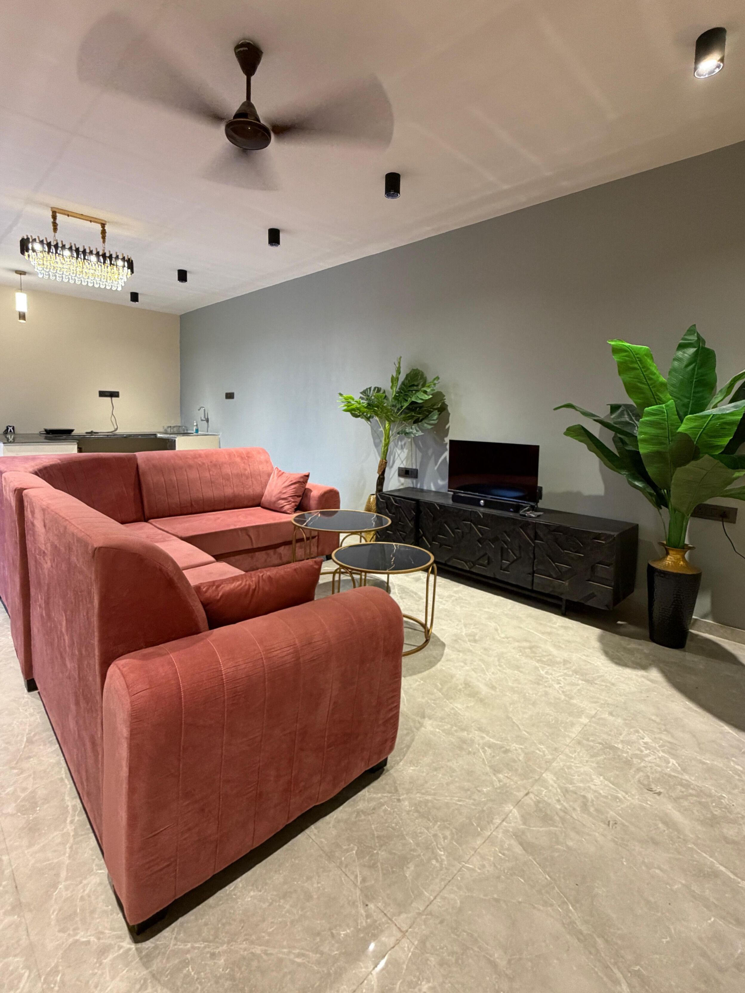 A modern living room with a sectional sofa, a small round table, a television on a black cabinet, and a ceiling fan.