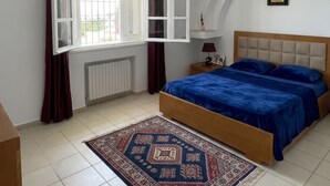 Ein Schlafzimmer mit einem Bett, einer Hängelampe, einem Fenster mit Vorhängen, einem Teppich und einer Heizung.