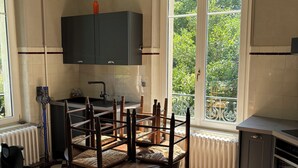 Una cocina con piso a cuadros, una mesa de comedor con sillas, una ventana con vista a follaje y un radiador.