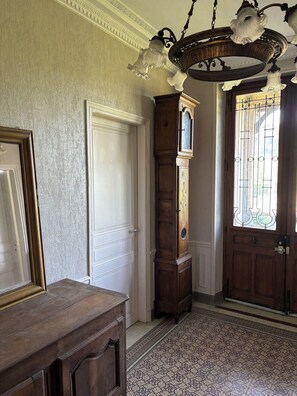 A hallway with a wooden dresser, a tall grandfather clock, and a door with a metal gate. - Argonne Guesthouse (Dombasle-en-Argonne)
