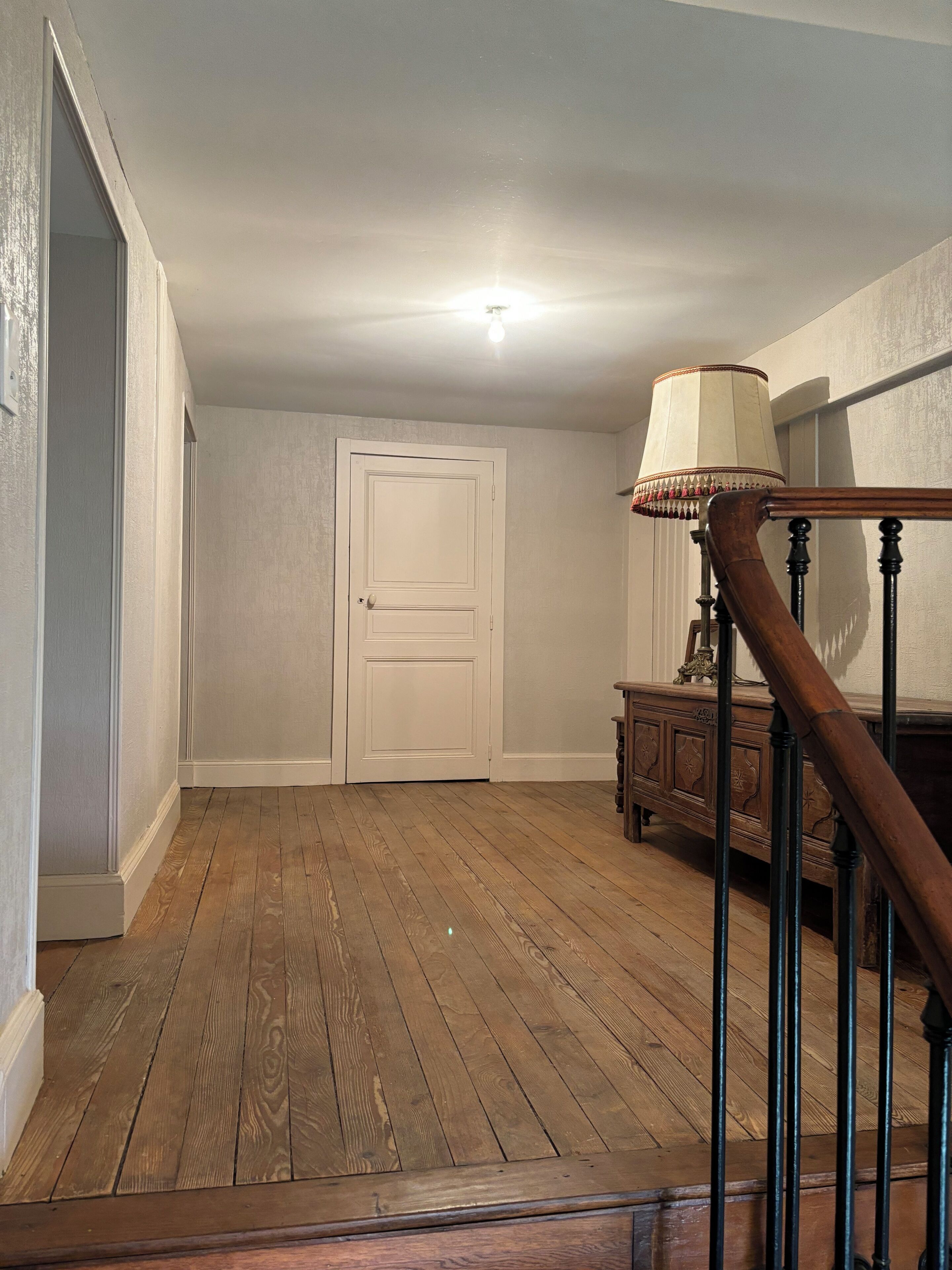 A wooden staircase with a lamp, a closed door, and a wooden floor.