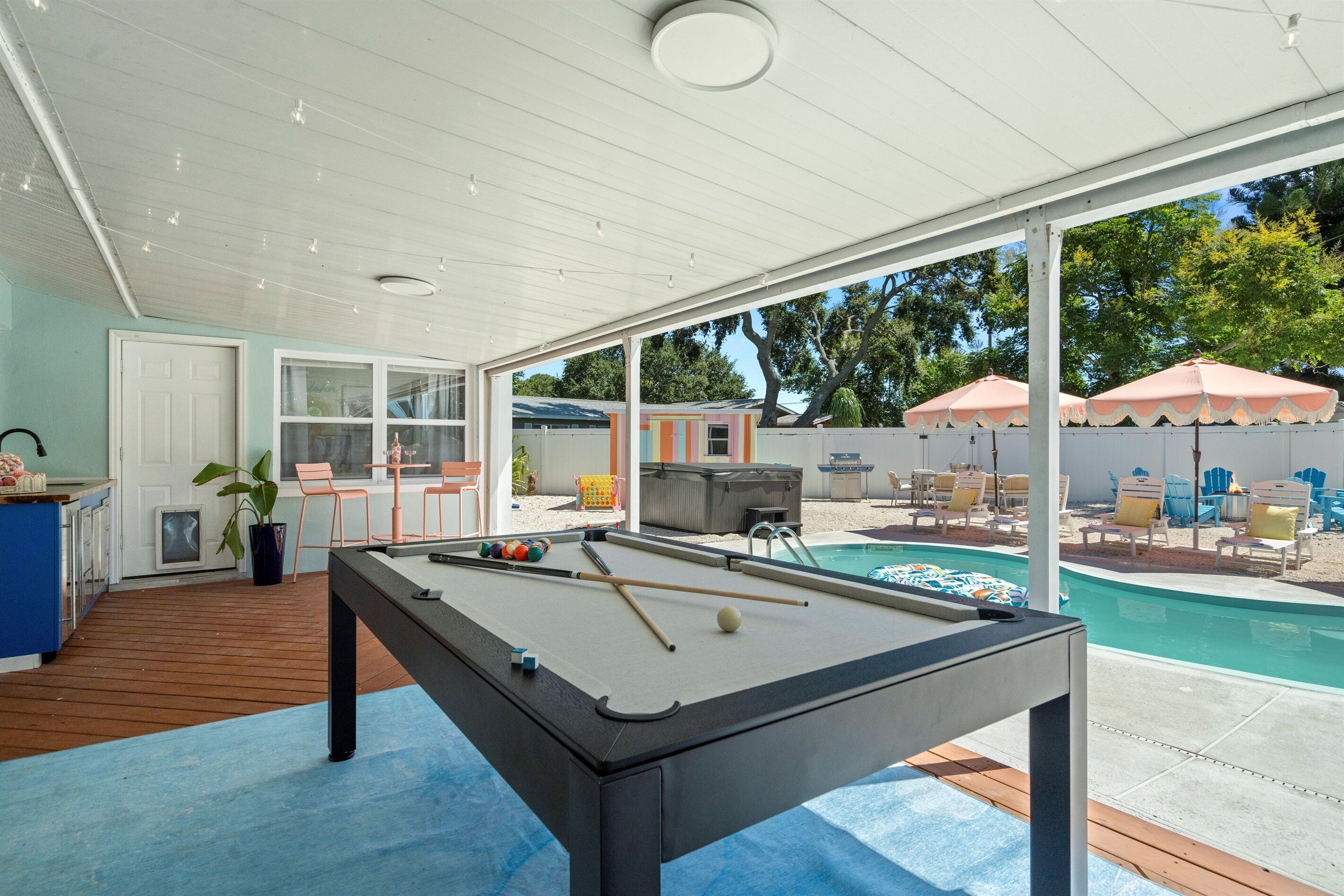 Mesa de billar en un espacio exterior cubierto con vista a una piscina y mobiliario de patio.
