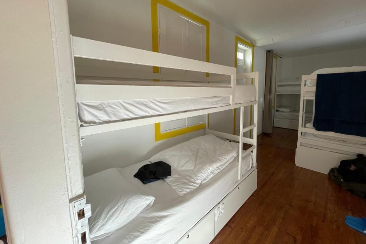Een slaapkamer met een stapelbed, houten vloer, witte muren en een deur.