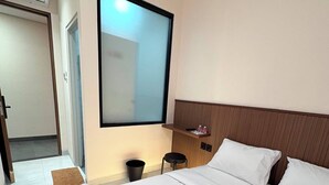 Quarto de hotel com cama, mesa de cabeceira, espelho, lixeira e porta.