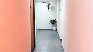 Um corredor com piso ladrilhado, um vaso de planta e um ventilador de teto.