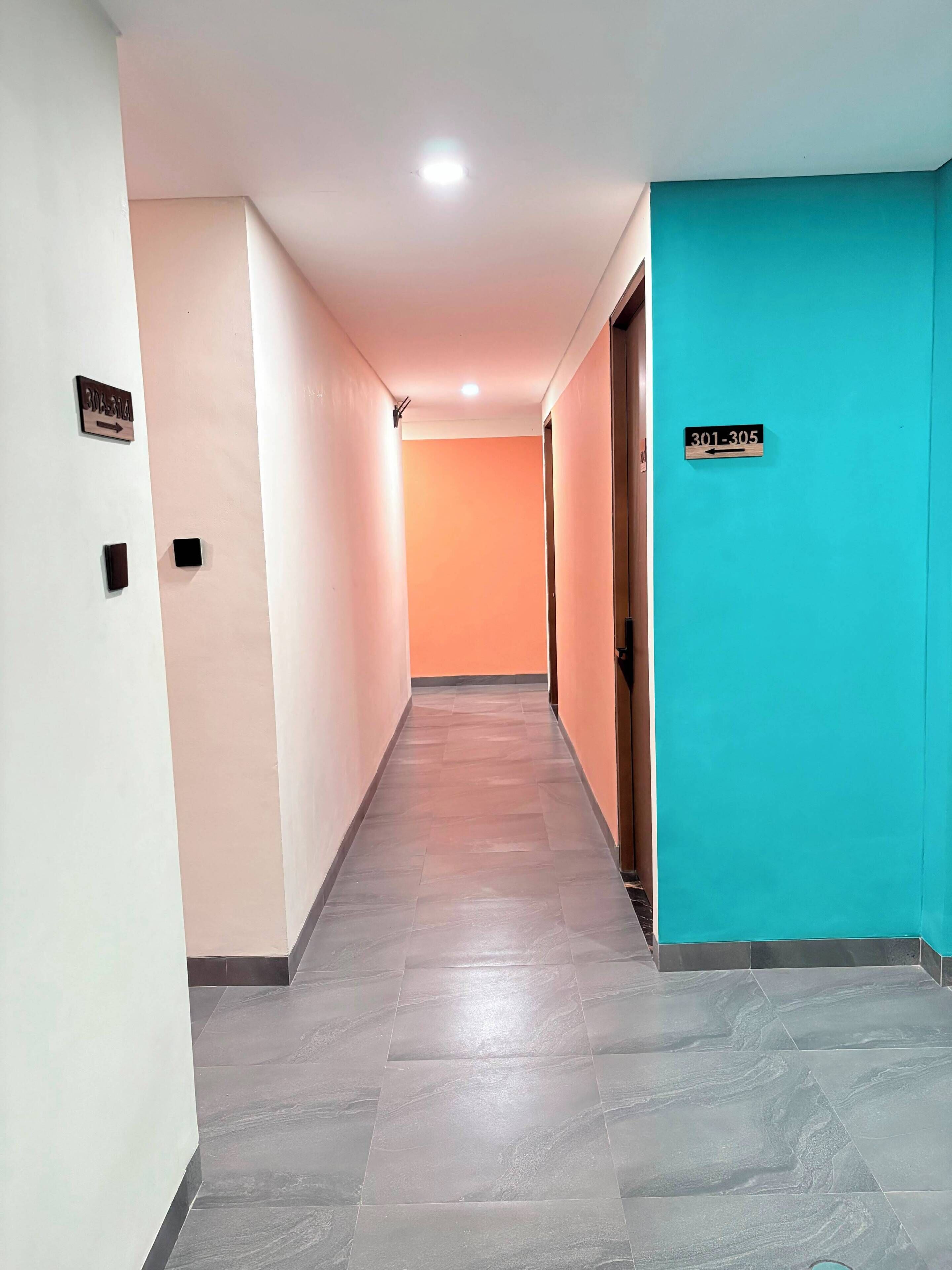 Un pasillo con indicaciones, una pared color turquesa y suelo de baldosas.