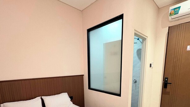 Habitación de hotel con cama, televisor montado en la pared, una puerta y una toalla pequeña sobre la cama.