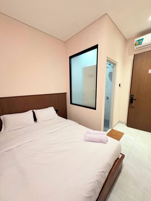 Habitación de hotel con cama, televisor montado en la pared, una puerta y una toalla pequeña sobre la cama.