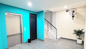 Un pasillo con suelo de baldosas, una escalera, una puerta y un ventilador fijado a la pared.