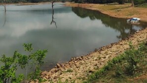 A calm lake with a boat on the shore, surrounded by trees and hills. - GaindaPhool Homestay, Chhichhli - Jashpur (Ganjenar)