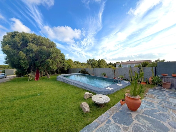 A backyard with a swimming pool, a red slide, and a stone patio.