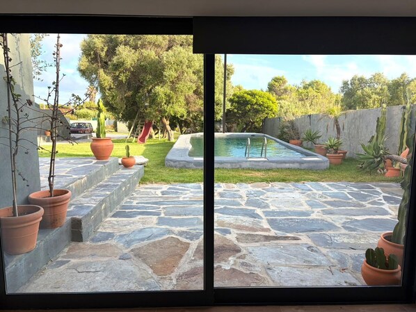A stone patio leading to a swimming pool with potted plants and a grassy area.