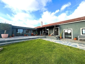 A modern house with a patio, large potted plants, and a well-maintained lawn.