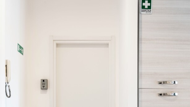 Una porta bianca con estintore e telefono a parete, un piccolo segnale di uscita di sicurezza e una cassetta di pronto soccorso sulla porta.
