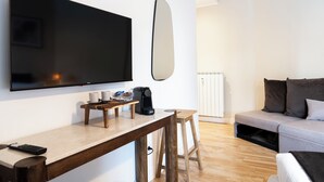 Un soggiorno moderno con TV a schermo piatto montata a parete, una macchina per il caffè, un piccolo tavolino e un divano con cuscini.