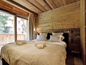 Ein Schlafzimmer mit einem hölzernen Kopfende, einem großen Bett mit vielen Kissen, einem Nachttisch und einem Fenster mit Vorhängen.