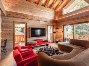 Ein gemütliches Blockhaus-Interieur mit einem großen Fernseher, Holzwänden, einem roten Sofa und einem großen Fenster mit Blick ins Freie.