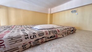 Una cama individual con una colcha estampada en una habitación con paredes color beige y un ventanal pequeño.