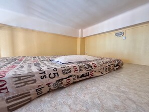 Ein Einzelbett mit einem gemusterten Überwurf in einem Zimmer mit beigen Wänden und einem kleinen Fenster.