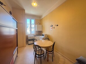A compact kitchen with a dining table and chairs, a refrigerator, and a window with a view of buildings. - Apartment 20m from the beach - 4 guests (Les Sables-d'Olonne)