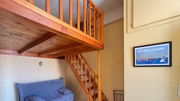 Una habitación con escalera de madera, un sofá azul, una mesita y un cuadro en la pared.