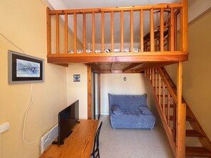 Una habitación con una cama nido de madera, un escritorio con una computadora, una silla, un sofá y una escalera.