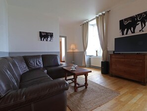 Een woonkamer met een leren bank, een houten salontafel, een televisie op een houten kast en een schilderij aan de muur.
