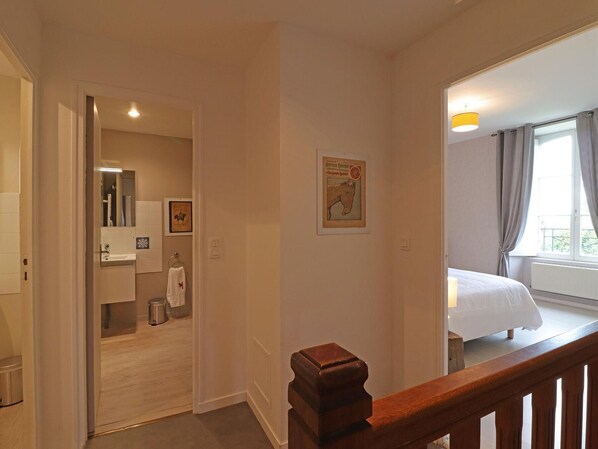 Hotelkamer met een bed, een raam met gordijnen, een houten leuning en een badkamer met wastafel en spiegel.