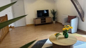 A living room with a television, a sofa, a coffee table with flowers, and a plant.