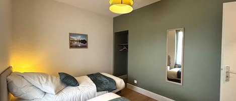 Une chambre avec deux lits, un luminaire suspendu, un placard et un miroir au mur.