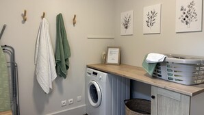 A laundry room with a washing machine, drying rack, and hanging towels.