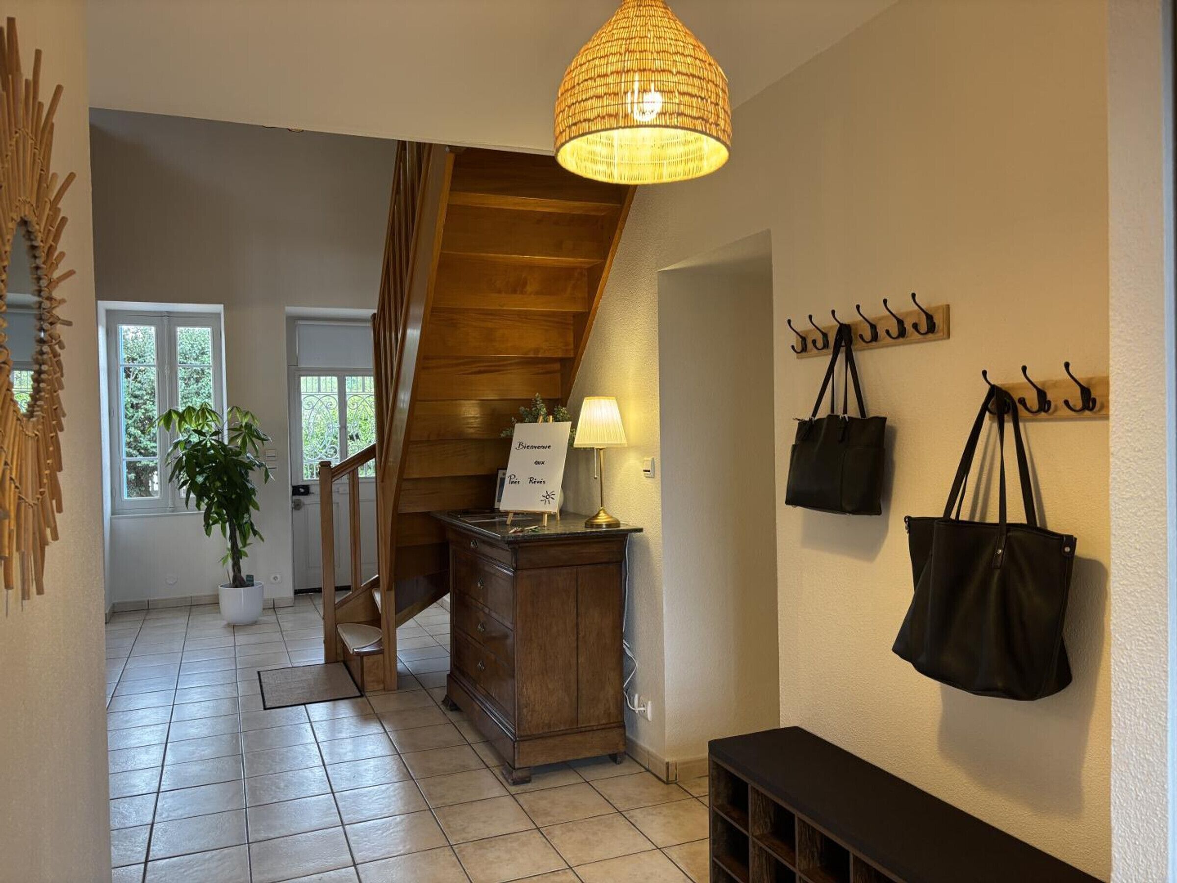 A hallway with a wooden staircase, a lamp, a sign, and a wall-mounted coat rack with bags.