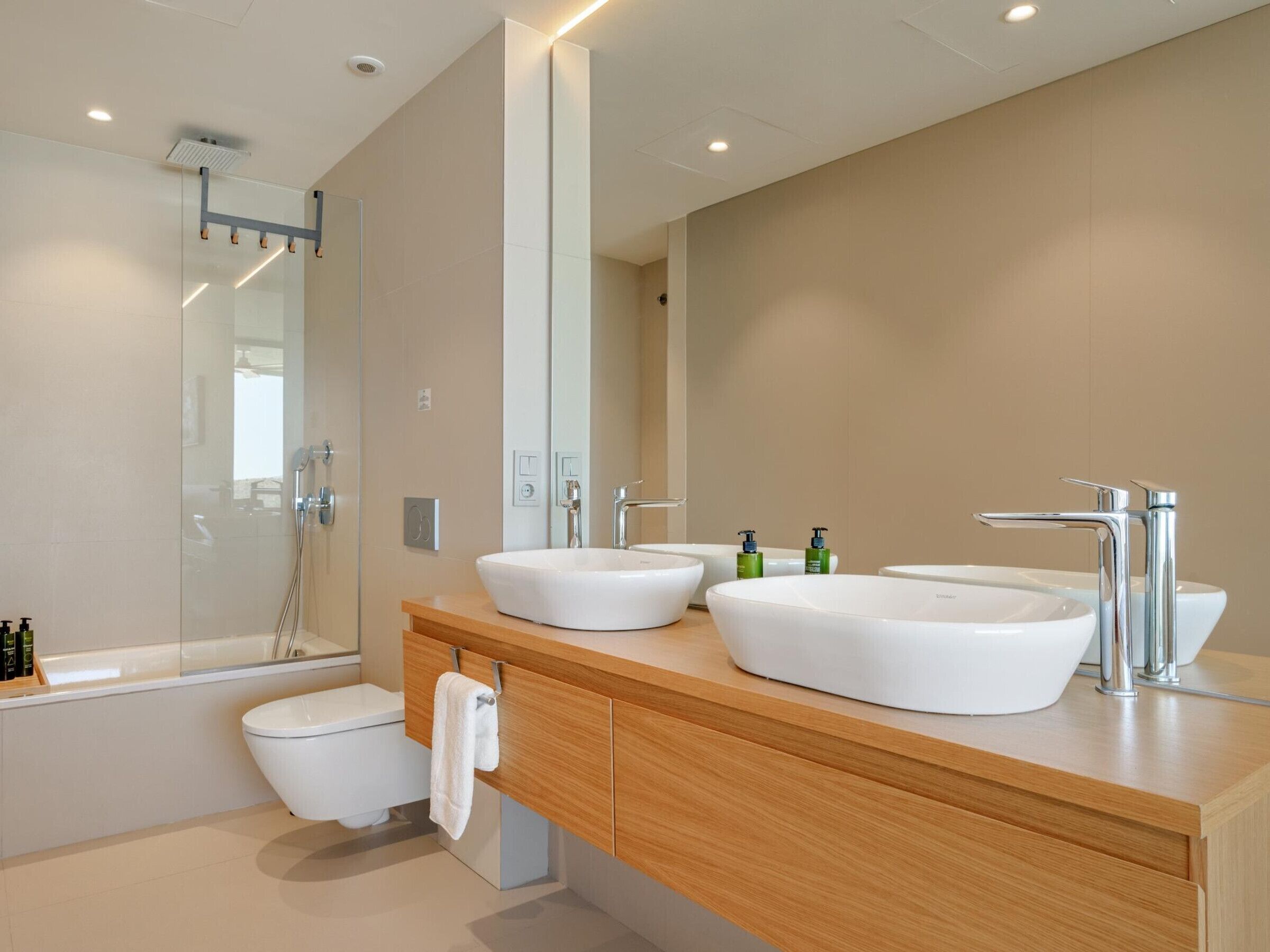 A modern bathroom with a double sink, a toilet, and a shower.