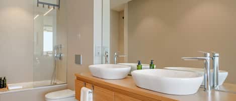 A modern bathroom with a double sink, a toilet, and a shower.