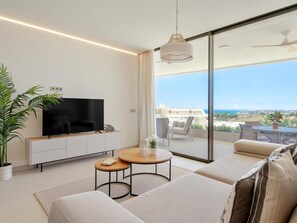 A modern living room with a flat-screen TV, a sofa, a coffee table, and a balcony with a view. - Bright apartment in tranquil area - 4 guests (Fuengirola)