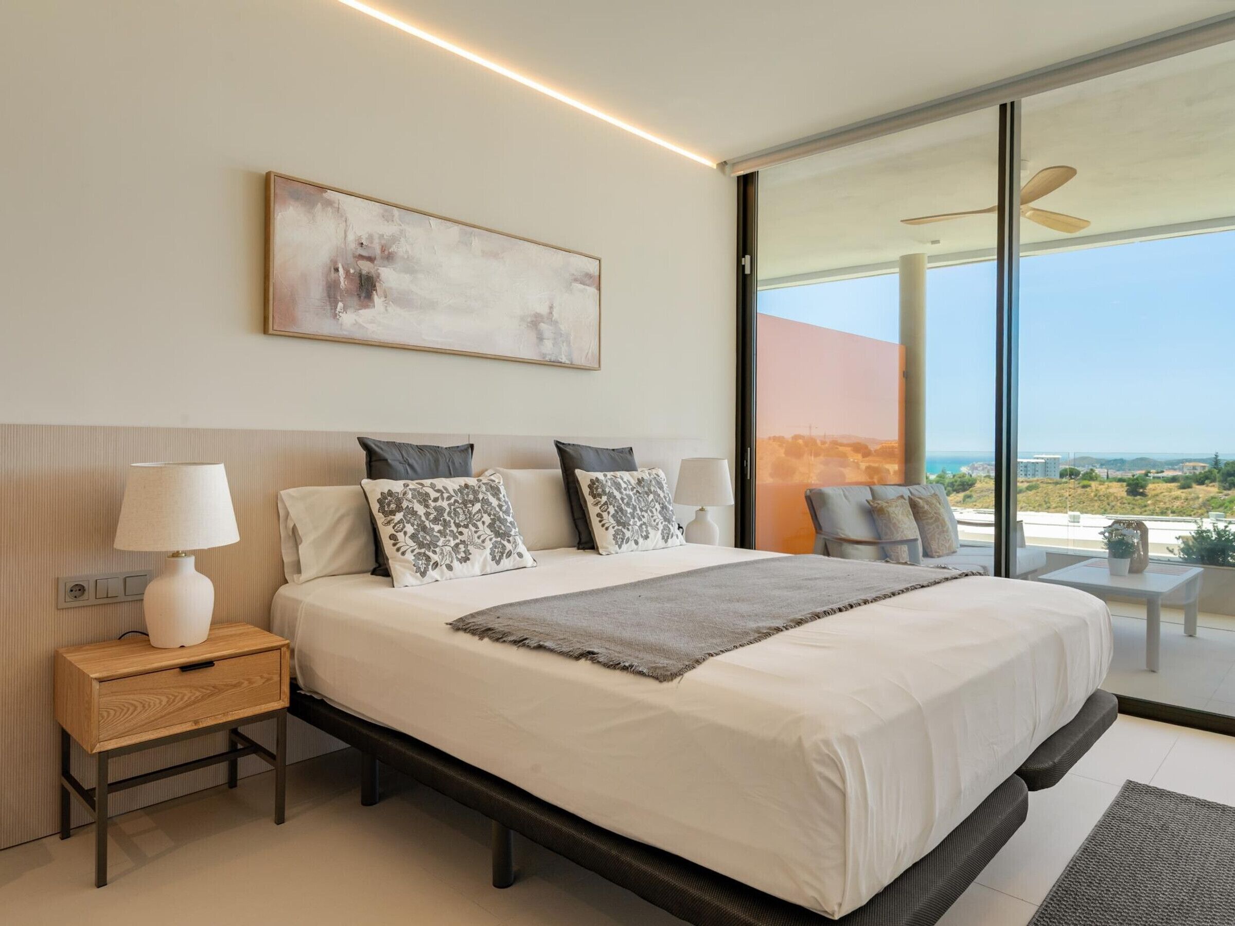Un dormitorio moderno con una cama grande, mesitas de noche, una lámpara de pie y vistas al exterior.