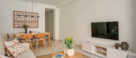 A modern living room with a sofa, coffee table, TV, and a dining area with chairs and a table.