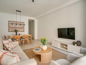 Ein modernes Wohnzimmer mit einer Couch, einem Couchtisch, einem Fernseher und einem Essbereich mit Stühlen und einem Tisch.