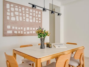 A dining area with a wooden table, six chairs, a vase with flowers, a book, and a modern light fixture. - Stylish apartment in Soho Malaga - 6 guests (Málaga)
