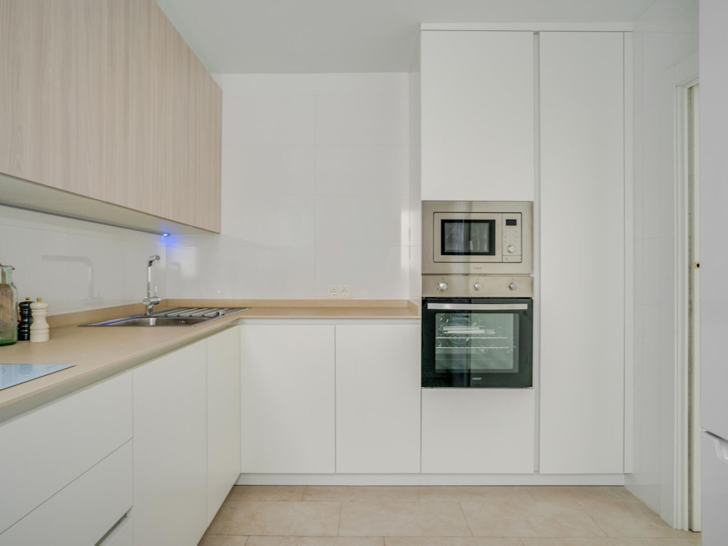 Eine moderne Küche mit weißen Schränken, einer Edelstahlspüle, einer Mikrowelle und einem Backofen.