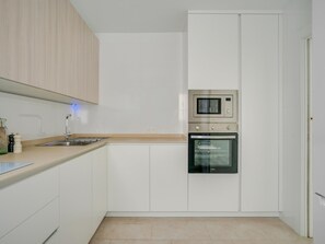 Eine moderne Küche mit weißen Schränken, einer Edelstahlspüle, einer Mikrowelle und einem Backofen.