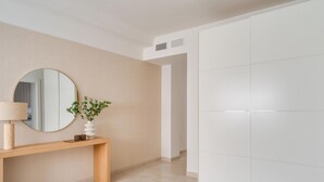 Ein schlicht eingerichteter Raum mit einem Holzkonsolentisch, einem runden Spiegel und einem weißen Kleiderschrank.