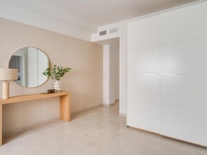 Ein schlicht eingerichteter Raum mit einem Holzkonsolentisch, einem runden Spiegel und einem weißen Kleiderschrank.