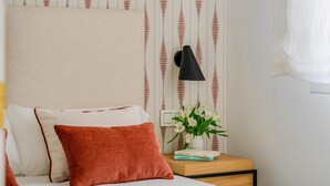 Ein Schlafzimmer mit einem Bett, Kissen, einem Nachttisch mit Lampe, einer Blumenvase und floraler Tapete.