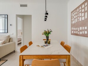 Een moderne eethoek met een marmeren tafel, houten stoelen, een vaas met bloemen en een groot abstract schilderij aan de muur.